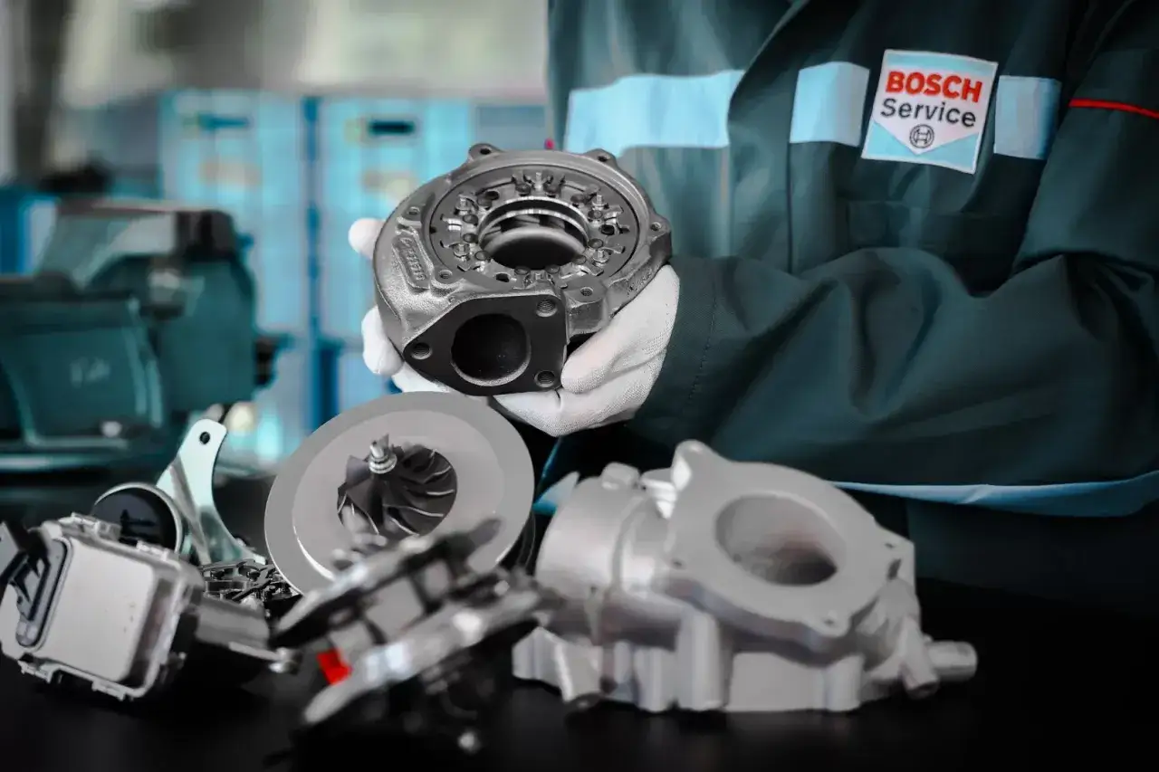 Mechanik w fartuchu Bosch Service prezentuje części do regeneracji turbo.