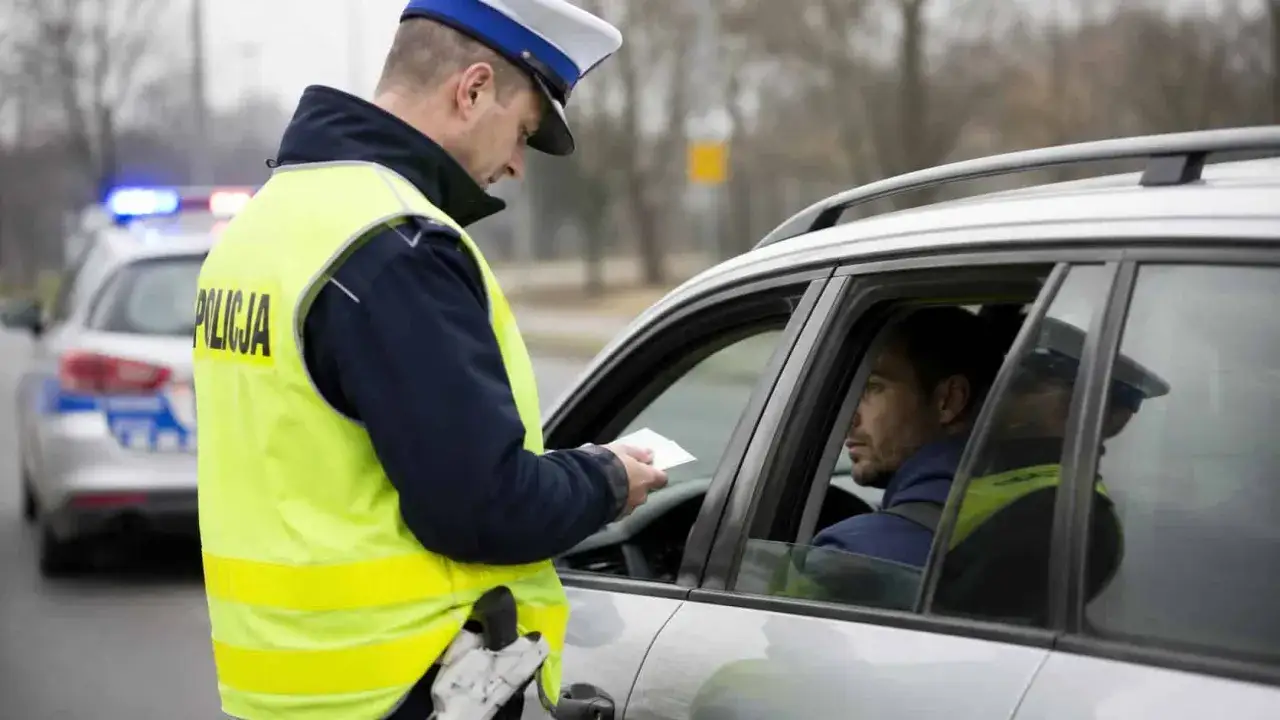 Policjant w kamizelce odblaskowej wręcza kierowcy notatkę. Może to być mandat, za kt&oacute;ry zabierają prawo jazdy na 3 miesiące.