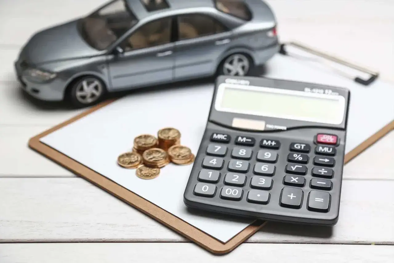 Model samochodu, stos monet i kalkulator sugerują rozważania o ubezpieczeniu samochodu powyżej 150 tys. netto czy brutto.