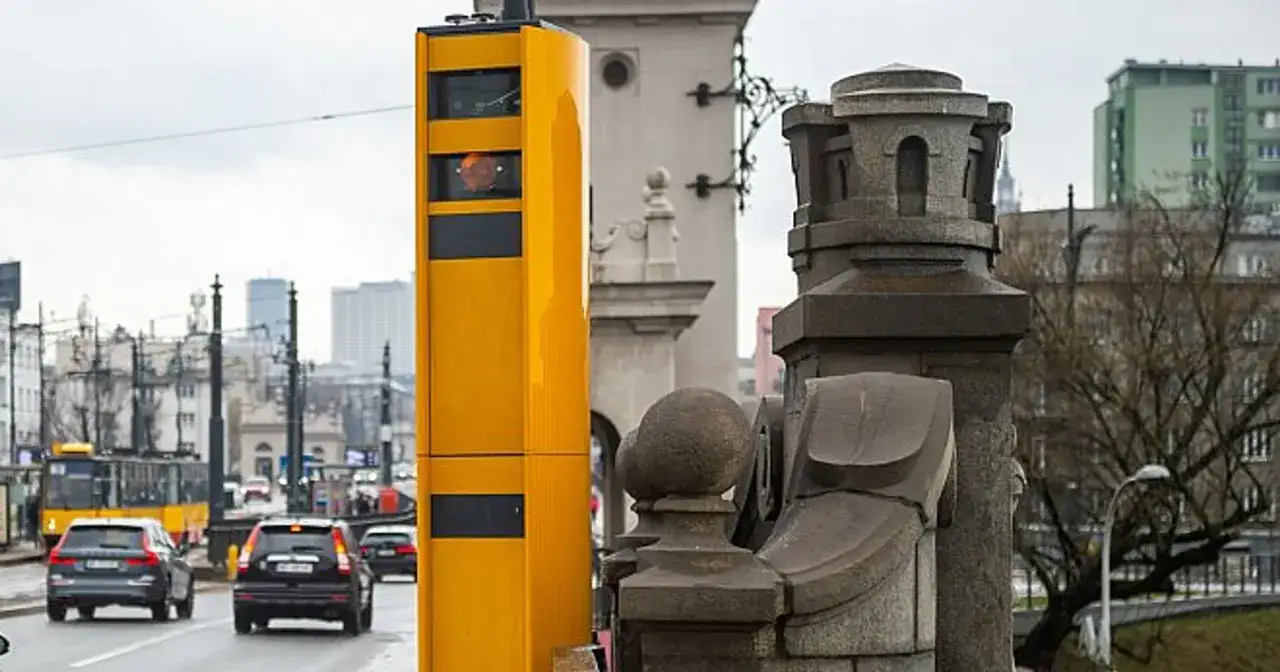 Ż&oacute;łty fotoradar stoi przy drodze, gotowy do rejestrowania prędkości. Z jakiej odległości łapie fotoradar? To zależy od jego ustawień.