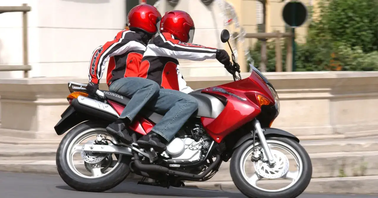 Dwie osoby w kaskach i kurtkach jadą na czerwonym motocyklu. Od ilu lat można robić prawo jazdy na motor 125?