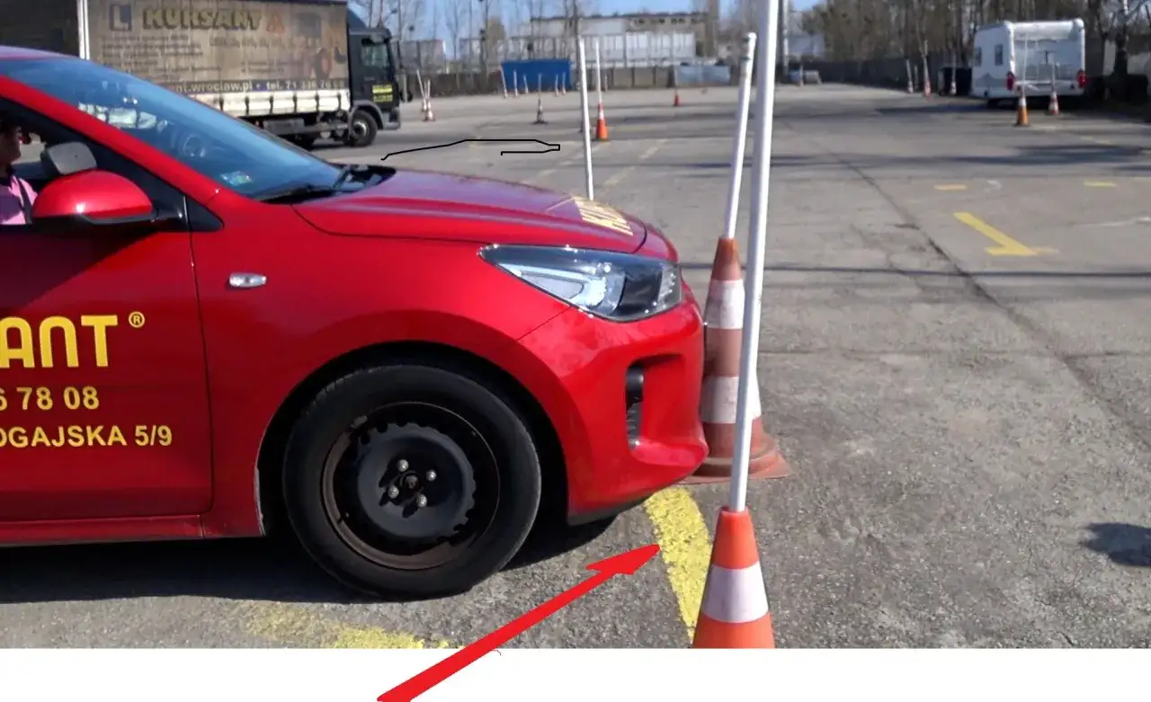 Czerwony samoch&oacute;d na placu manewrowym, obok pachołki. Może to być przykład dopuszczalnych błęd&oacute;w na egzaminie praktycznym na prawo jazdy.