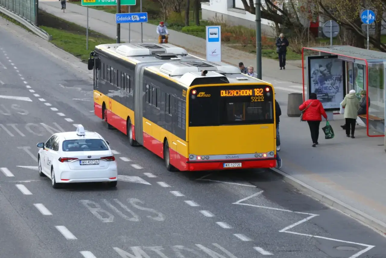 Autobus linii 182 zbliża się do przystanku, a biała taks&oacute;wka Uber czeka, sugerując, że autobus ma pierwszeństwo.