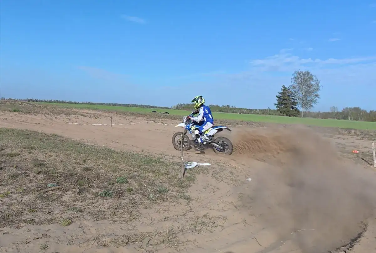 Motocyklista w kasku i stroju crossowym śmiga po piaszczystym torze, wzbijając tumany kurzu. Czy na crossa trzeba mieć prawo jazdy? To pytanie zadaje sobie wielu pasjonat&oacute;w.
