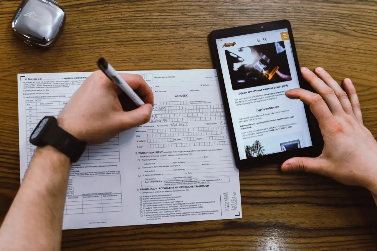 Wypełnianie wniosku o profil kandydata na kierowcę. Na stole leży formularz, długopis i tablet z informacjami o kursach.
